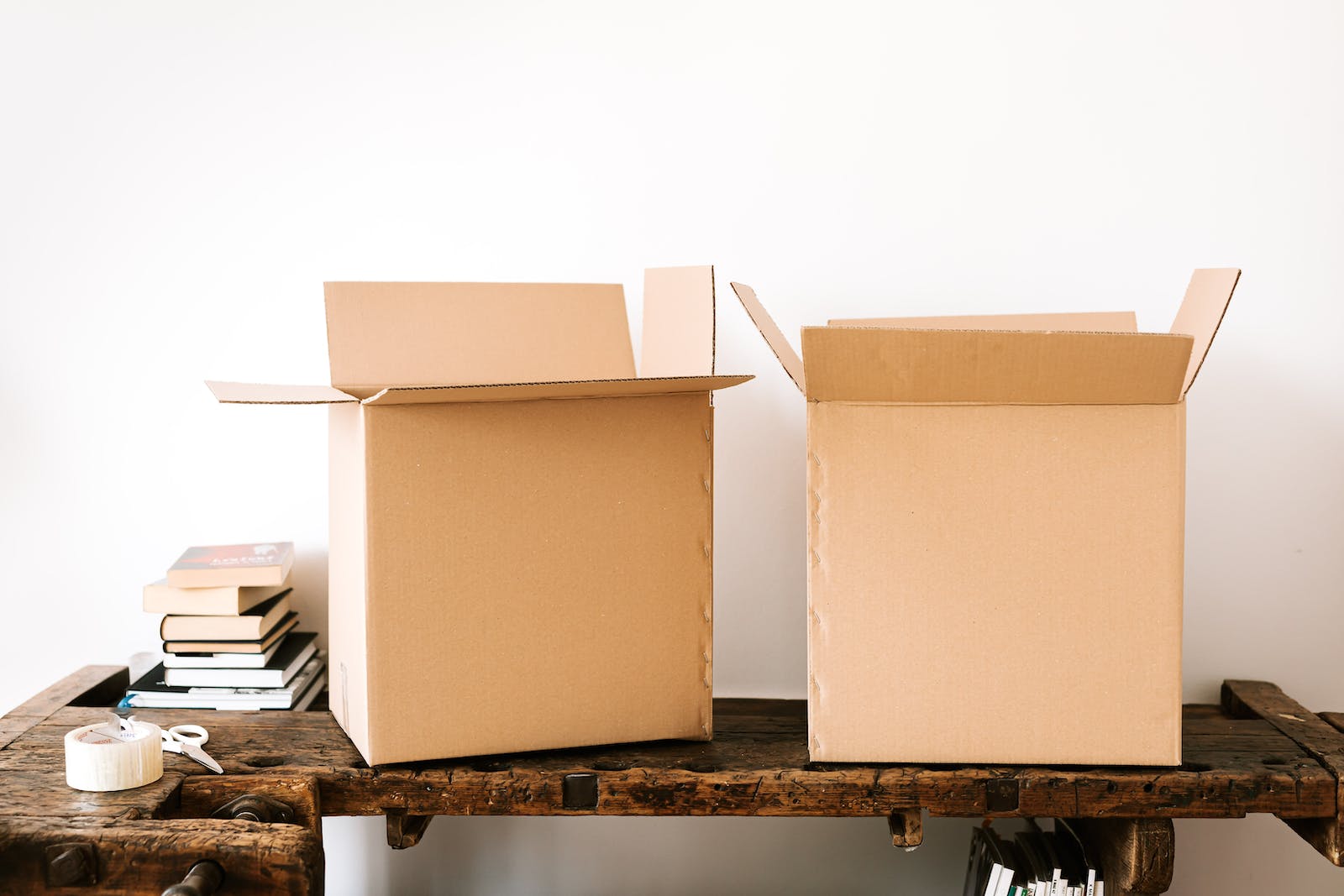 Opened carton boxes and stacked books placed on shabby wooden desk with tape against white wall